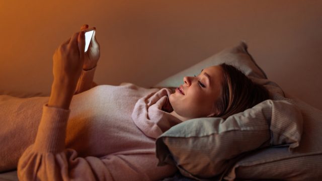 A young woman lying in bed while using her smartphone