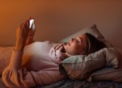 A young woman lying in bed while using her smartphone