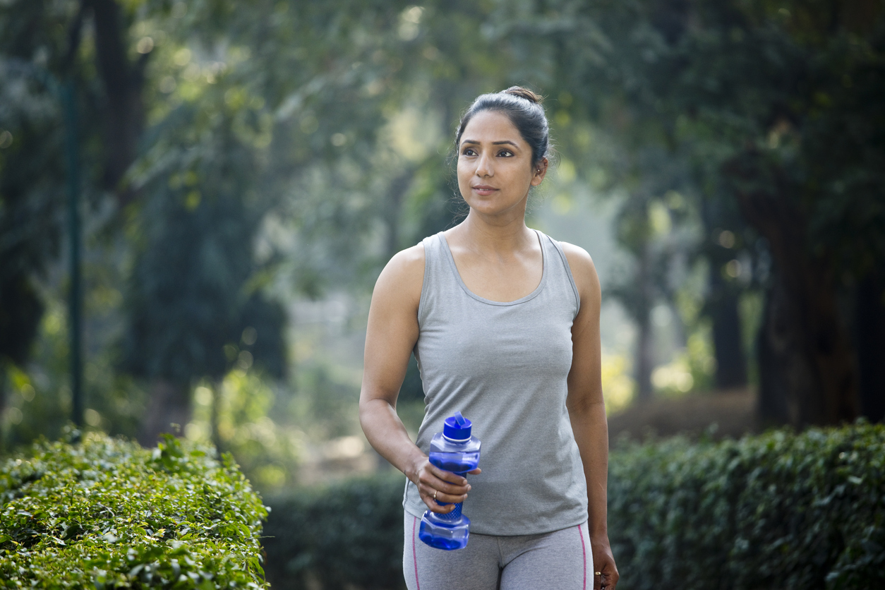 A young woman walking in the park while holding a water bottle.