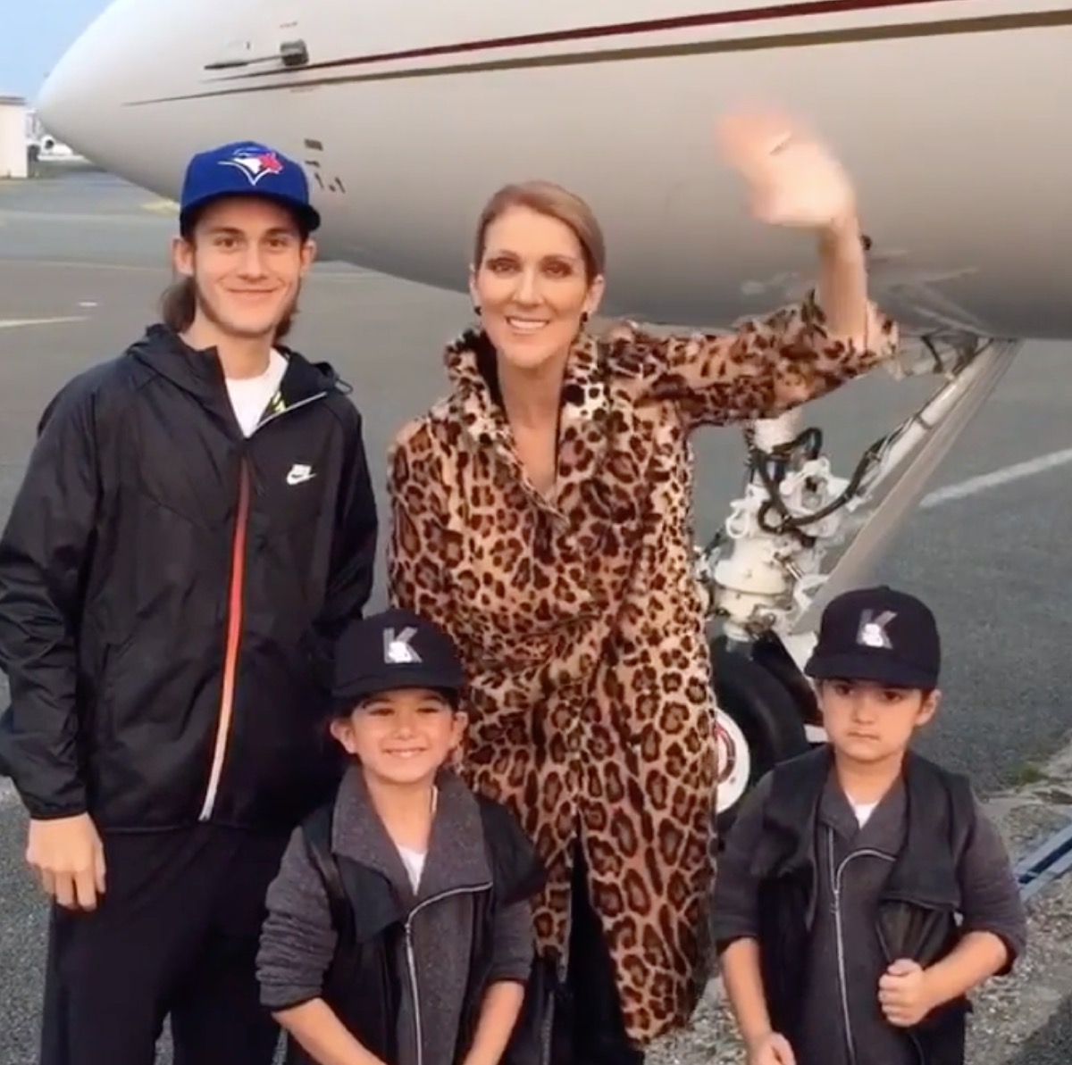 Celine Dion and sons waving in front of an airplane