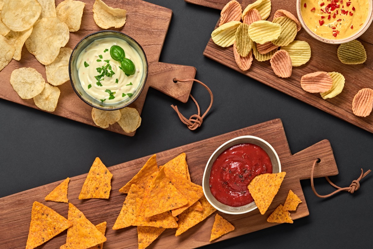 tortilla chips, potato chips, and veggie chips on wooden boards on a black table