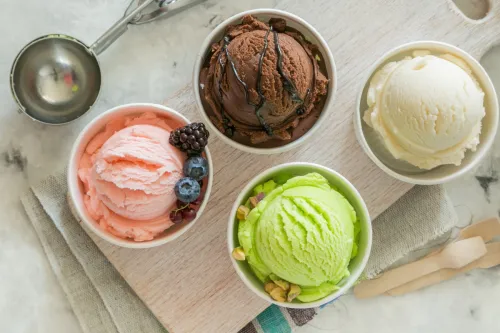colorful ice cream in paper cups next to metal scoop