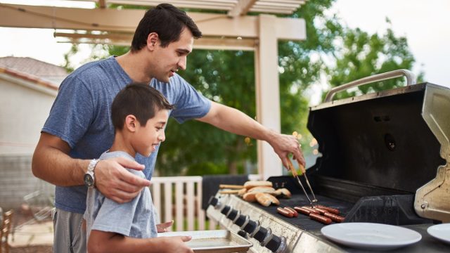 father teaching son how to grill hot dogs and bonding