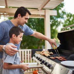 father teaching son how to grill hot dogs and bonding