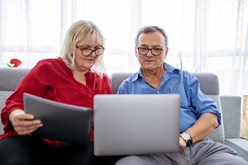 Senior, retired couple using a laptop, sitting on a couch together