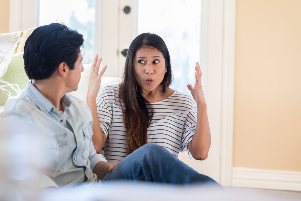 Eine aufgeregte Frau mitten in der Pubertät hebt frustriert die Hände, als sie zu Hause mit ihrem nicht wiederzuerkennenden Ehemann spricht.  Sie sitzen auf dem Wohnzimmerboden.