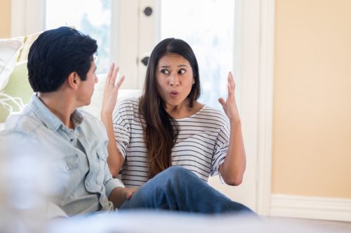 Một phụ nữ trung niên hoạt bát giơ tay tỏ vẻ thất vọng khi nói chuyện với người chồng xa lạ của mình ở nhà.  Họ ngồi trên sàn phòng khách của họ.