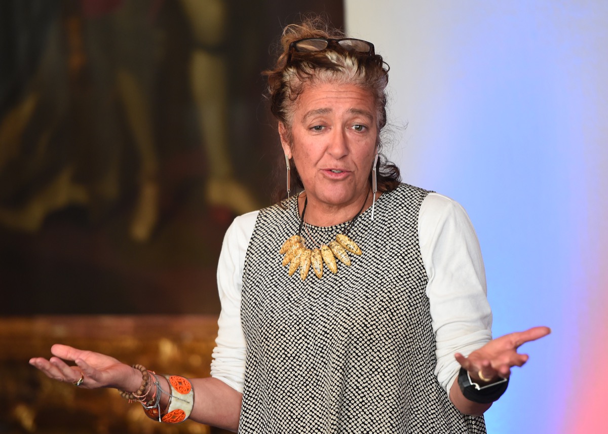 dame heather rabbatt in gray jumper and yellow necklace standing with arms out as if asking "what?"