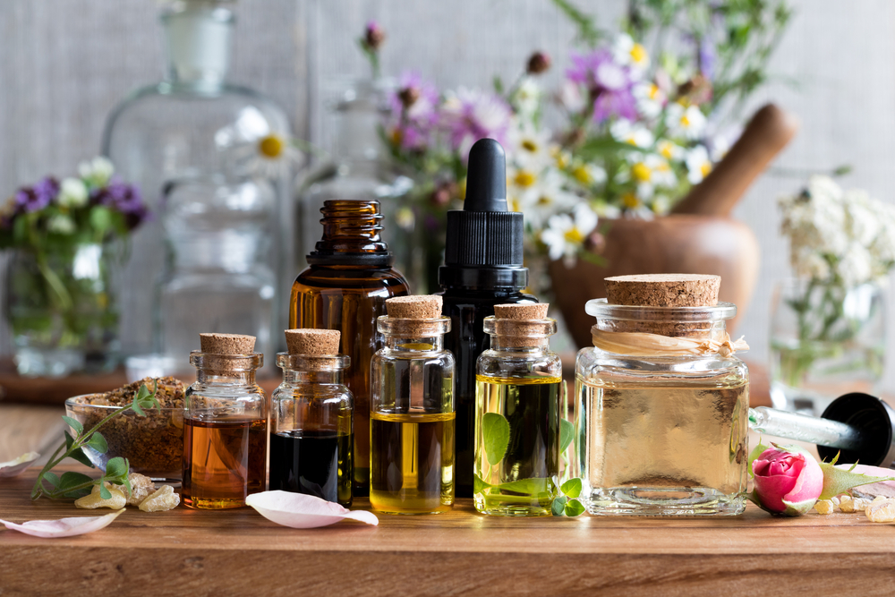 Bottles of various essential oils sitting on a table top with flowers in the background