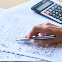 Close-up of unrecognizable woman working with tax return form: she checking papers and using calculator