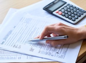 Close-up of unrecognizable woman working with tax return form: she checking papers and using calculator