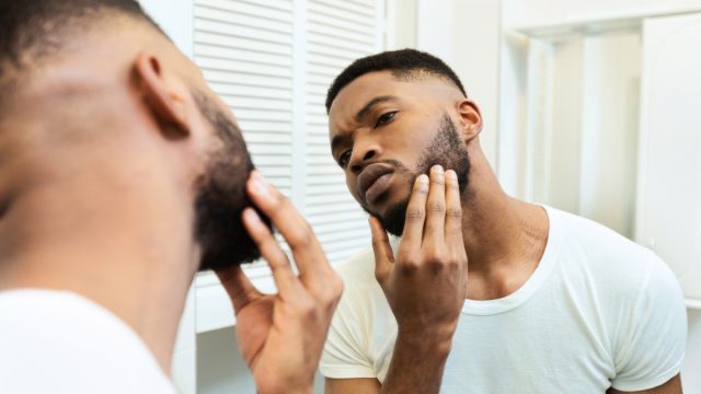 guy looking at his beard at bathroom mirror