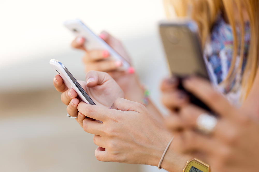 A shot of three people holding smartphones outdoors.