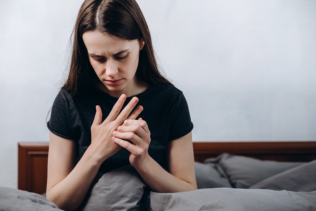 Young woman sitting up in bed holding her hand in pain