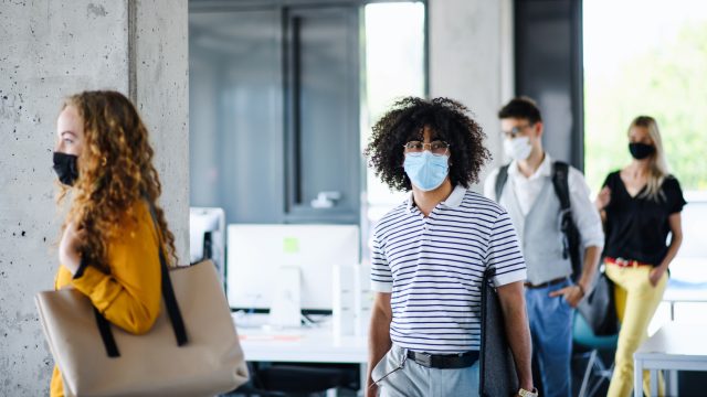 A group of young coworkers walk back into their office while wearing masks