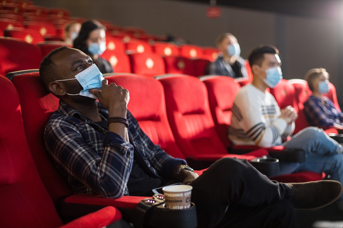 people sitting with masks inside a movie theater