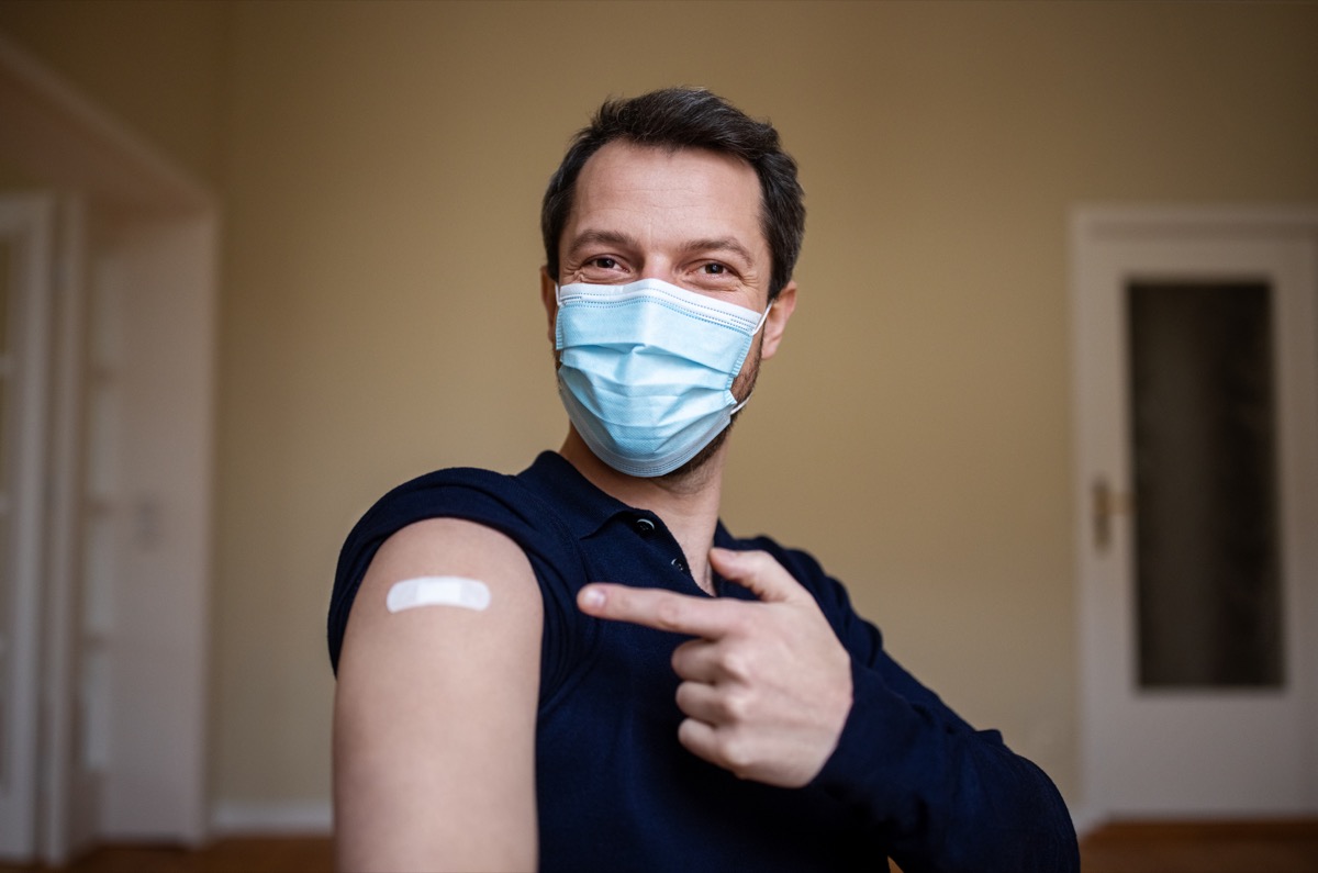 Man wearing protective face mask pointing at his arm with a bandage after receiving the covid-19 vaccine.