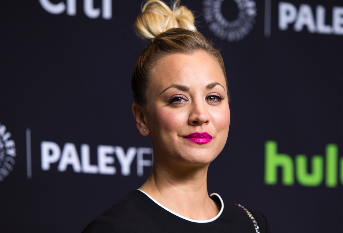 kaley cuoco with hair in a bun with pink lipstick in front of hulu step and repeat