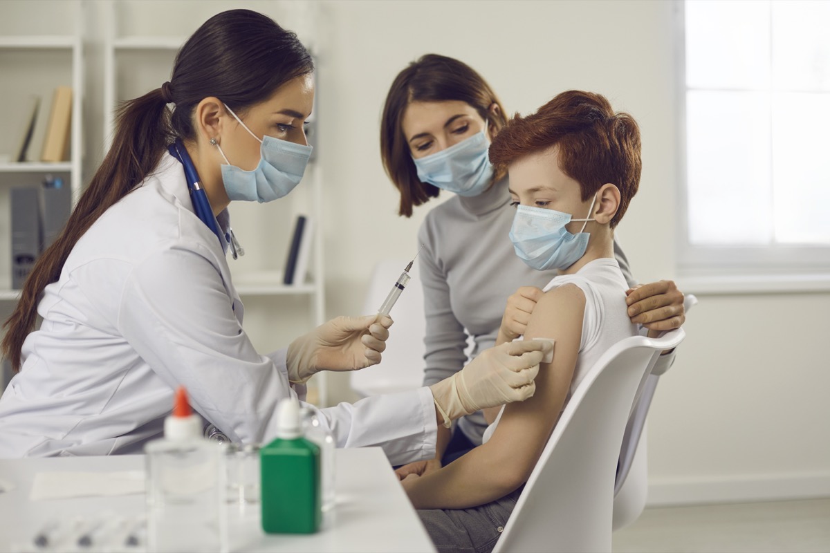 Woman doctor pediatrician nurse in medical protective mask wiping arm of teen boy patient before vaccination in medical clinic office. Vaccination and medicare concept