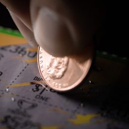 Extreme Close-Up of a Person's Hand Holding a Penny and Scraping a Scratch-Off Lottery Ticket