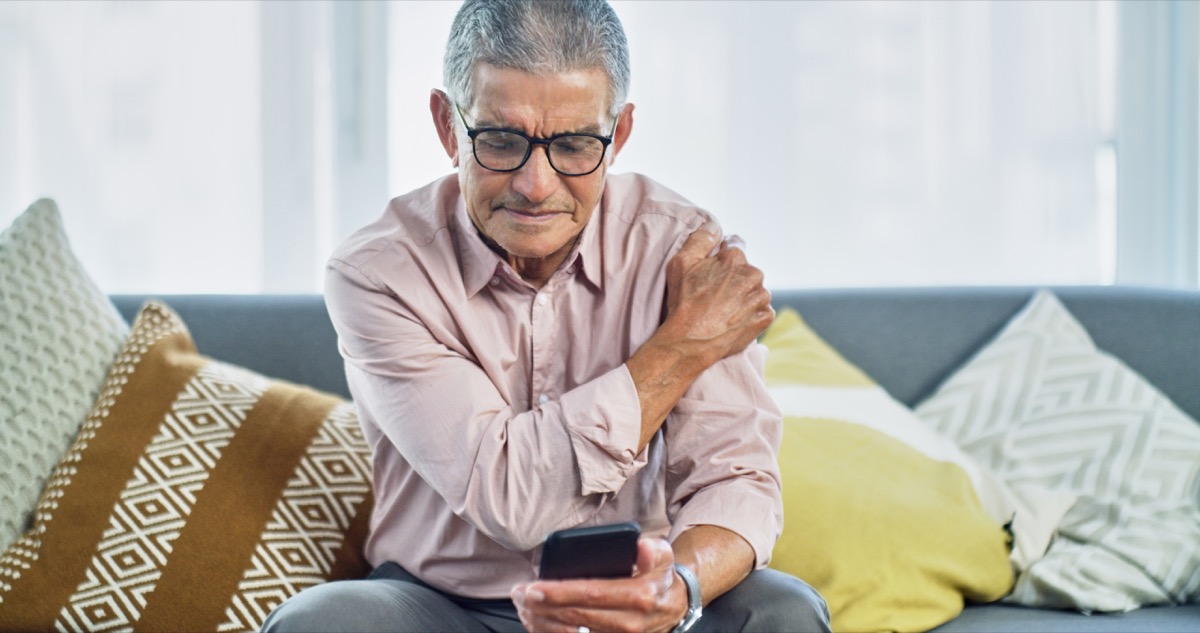 Shot of a senior man experiencing shoulder pain while using a smartphone at home