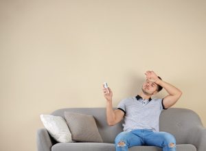 man sweating on couch holding air conditioner remote