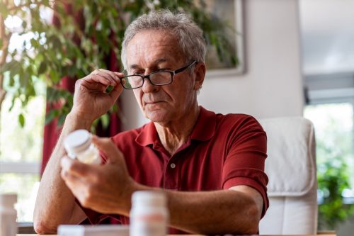 Alter Mann, der Nahrungsergänzungsmittel oder Medikamente betrachtet