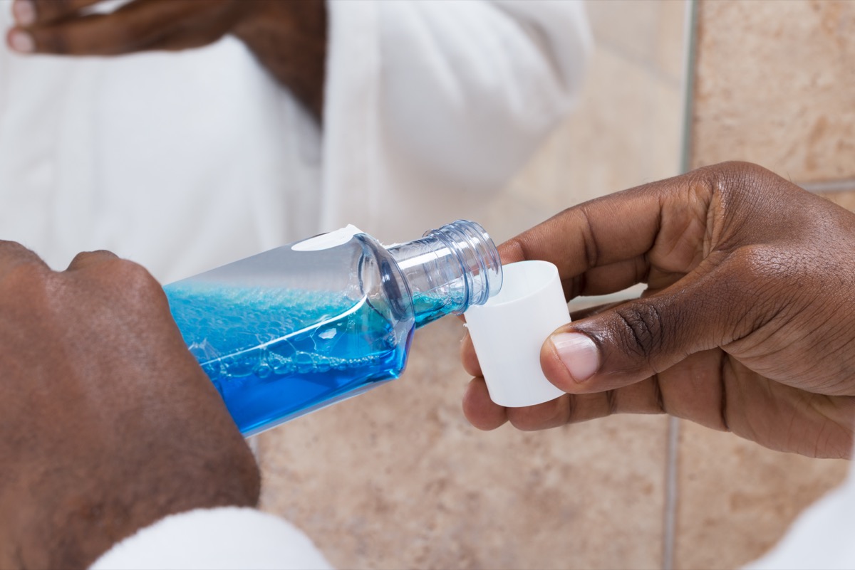 Close-up Of Person Hands Pouring Blue Mouthwash Into Bottle Cap