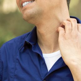 Close-up of man suffering itching scratching neck standing outdoors in a park