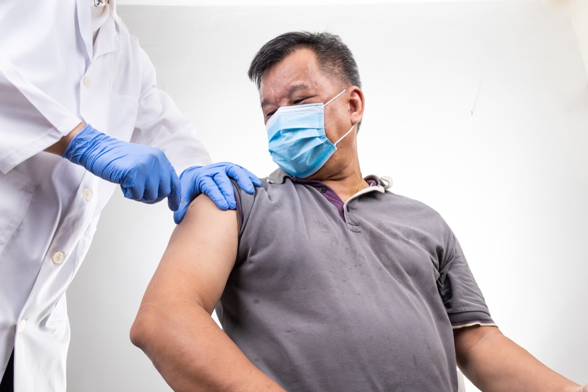 middle age man with face mask receiving Covid-19 vaccine injection onto the arm by medical practitioner