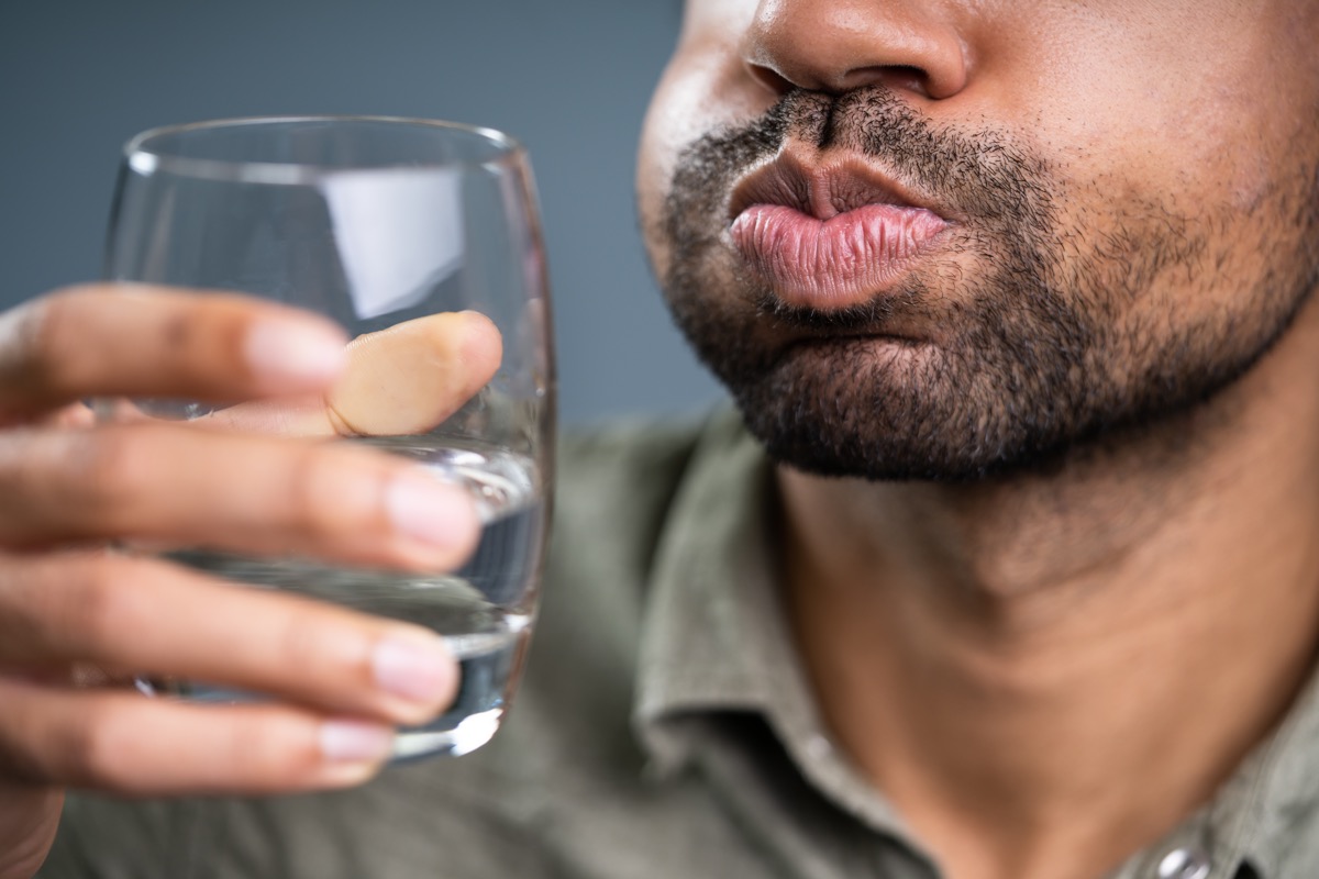 man swishing water in his mouth, holding glass