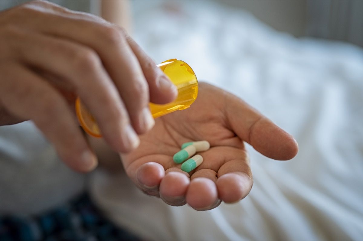 Closeup of man hand pouring capsules from a pill bottle into hand. Senior man taking daily medicine to consume. Close up of male hands taking daily dose of drug.