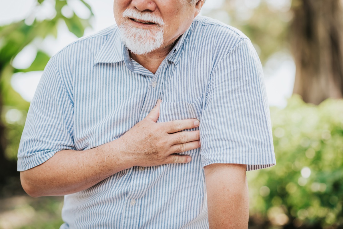 Cropped shot of senior man holding his chest and feeling pain suffering from heart attack outdoor at the park