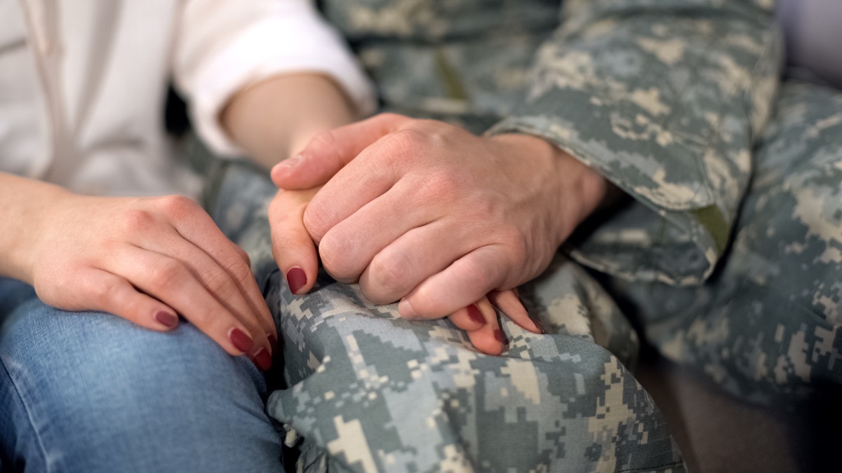Mannlig soldat som holder kjærestenes hånd, farvel før militærtjeneste, kjærlighet