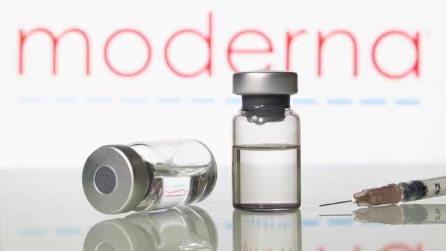 Two vials of vaccine and a syringe in front of the Moderna logo