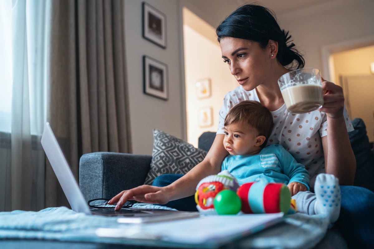 Young modern mother with a baby using laptop at home