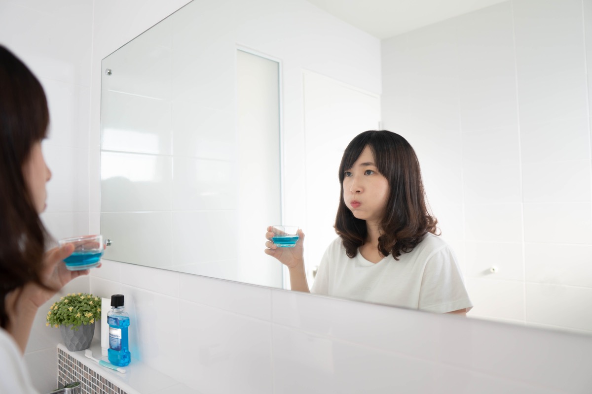 woman rinsing and gargling mouth with mouthwash after brushing her teeth in bathroom.