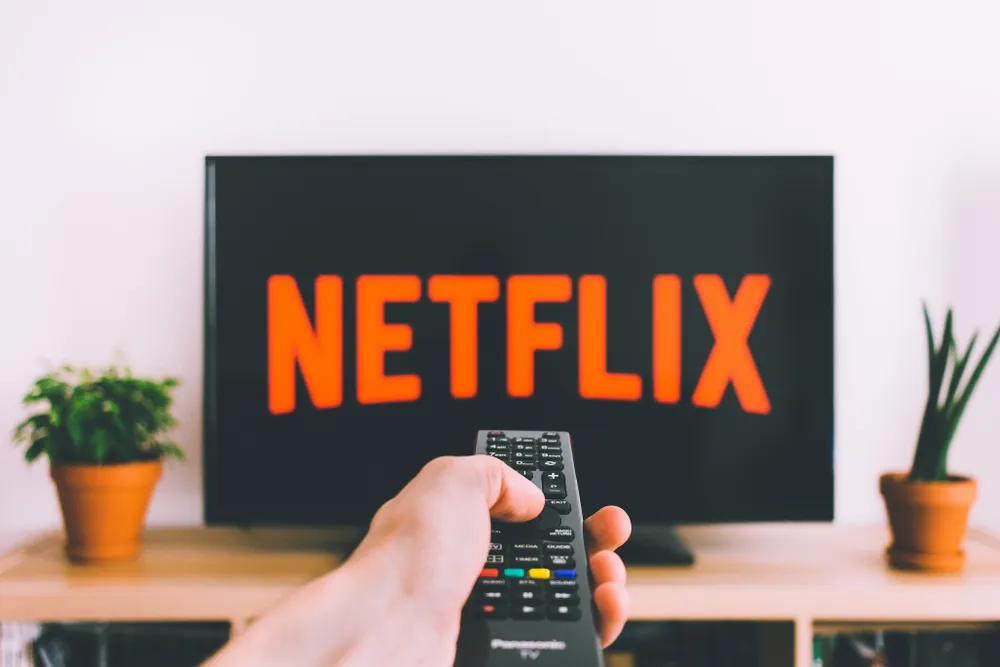 A person points the remote control at a TV with the Netflix logo