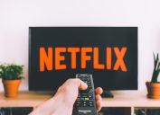 A person pointing a remote control at a TV with the Netflix logo on it