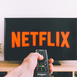 A person pointing a remote control at a TV with the Netflix logo on it