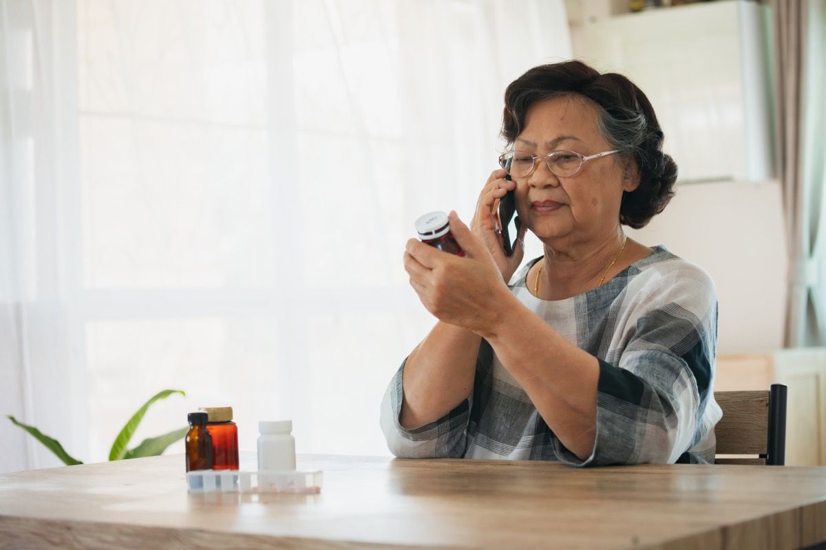 older woman making phone call while looking at pill bottle