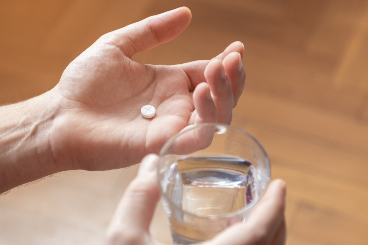 Hands holding a glass of water and a pill