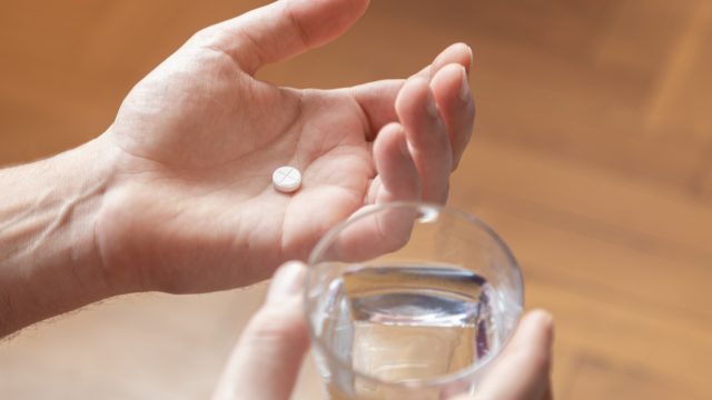 Hands holding a glass of water and a pill