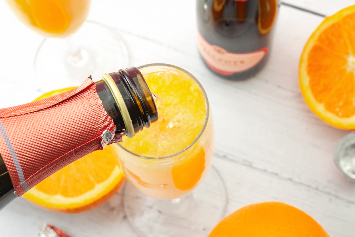 closeup of champagne being poured into mimosa