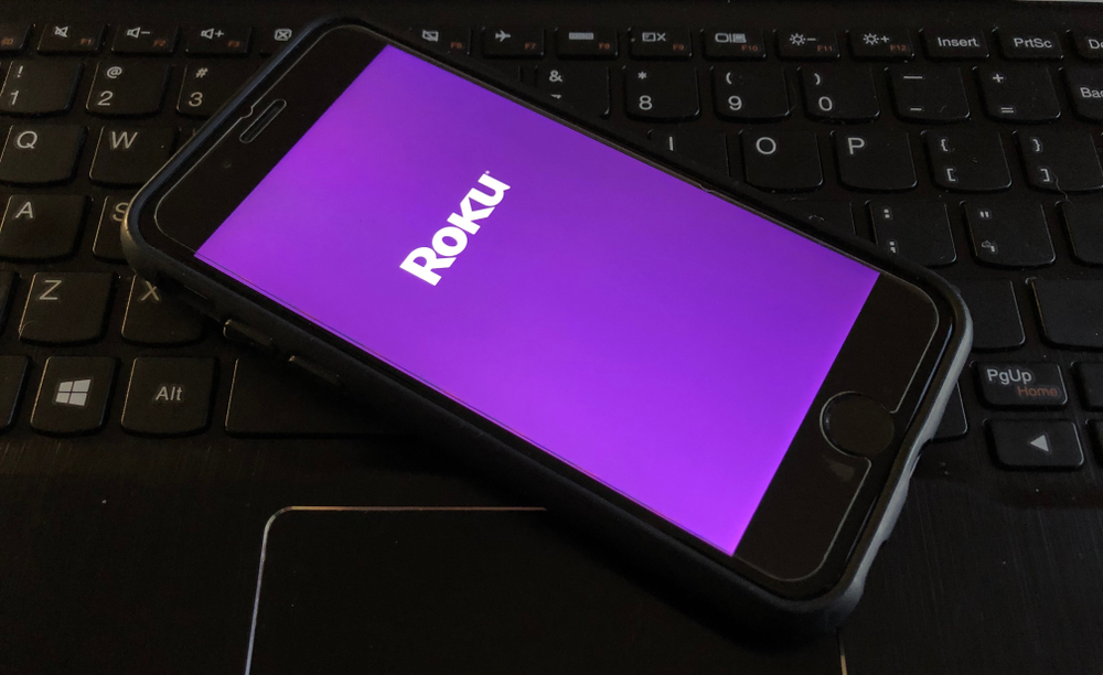 A phone loading the Roku app while resting on top of a keyboard
