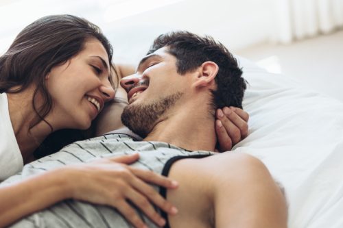 young couple smiles at each other under the covers