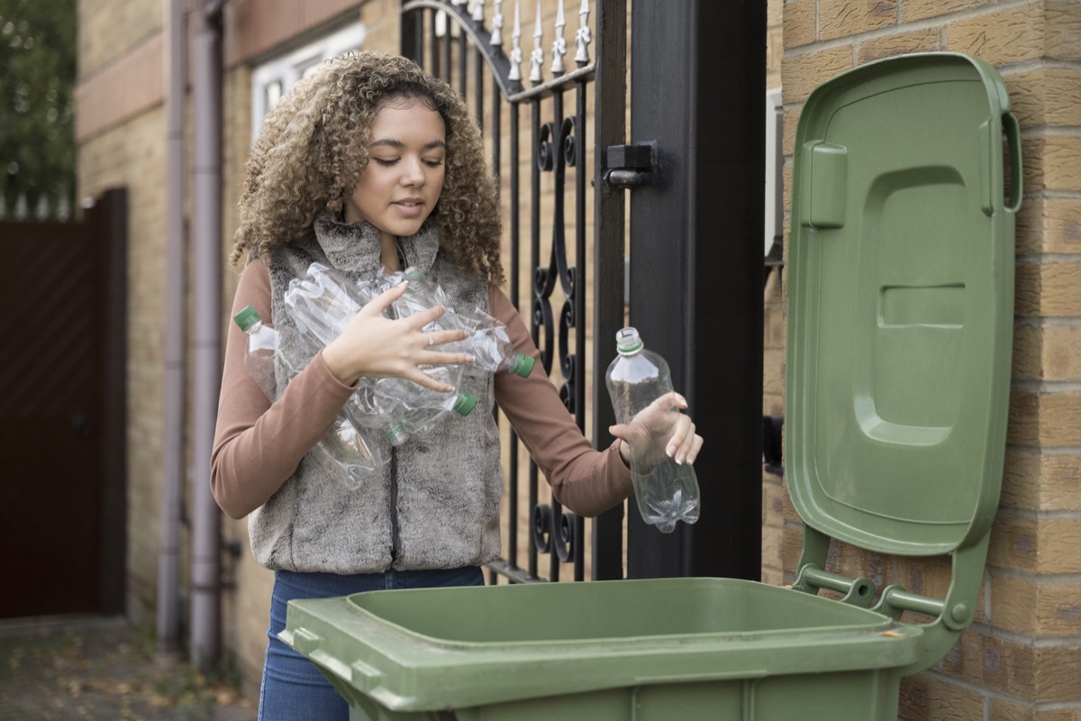 carrying armful of plastic bottles and placing them in recycling bin outside family home.