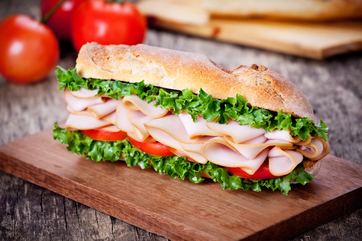 turkey sandwich with lettuce and tomato on a wooden board