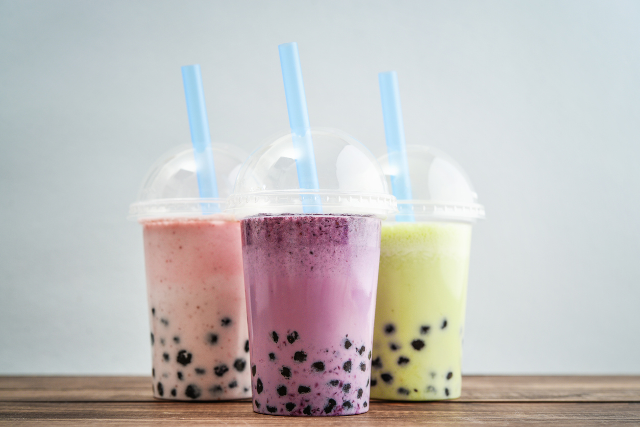 The flavors of bubble tea in plastic cups sitting on a table top.