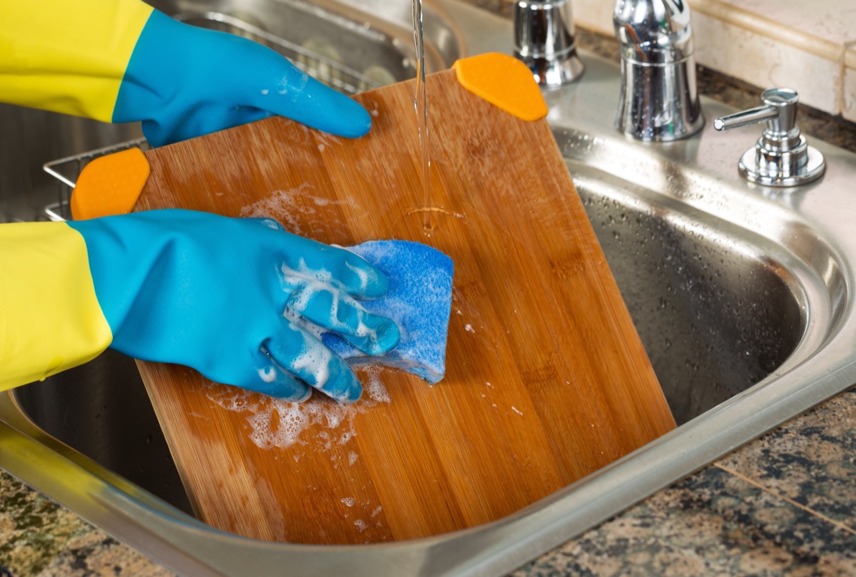 person wearing rubber gloves washing cutting board with soap